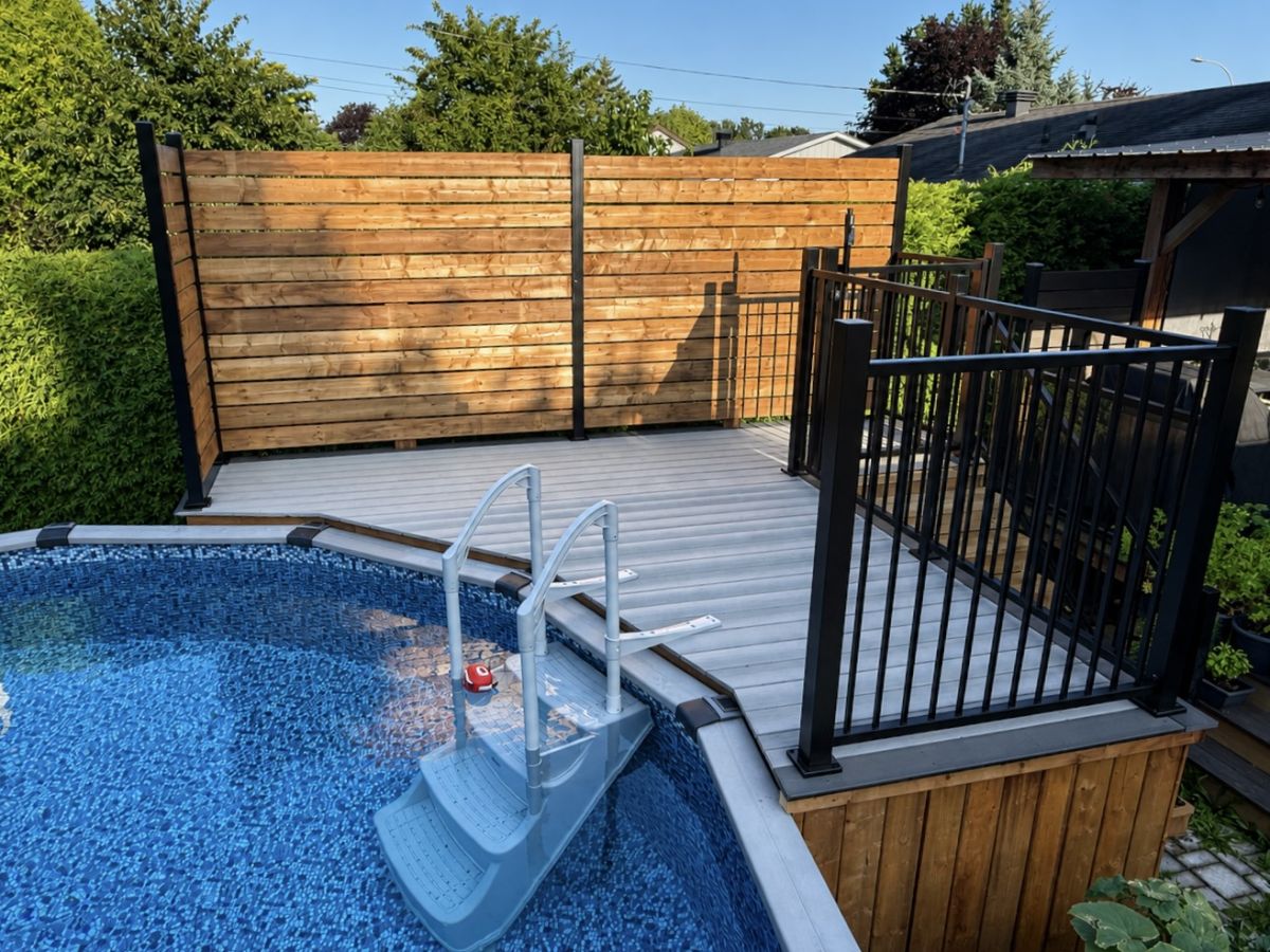 Patio Naturo-Deck gris autour d'une piscine hors terre, avec garde-corps noir et écran d'intimité en bois